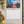 Load image into Gallery viewer, A January wall calendar hanging on a light beige wall in a kitchen setting, featuring a colorful city skyline sunset print on the top half and a white monthly grid on the bottom half.
